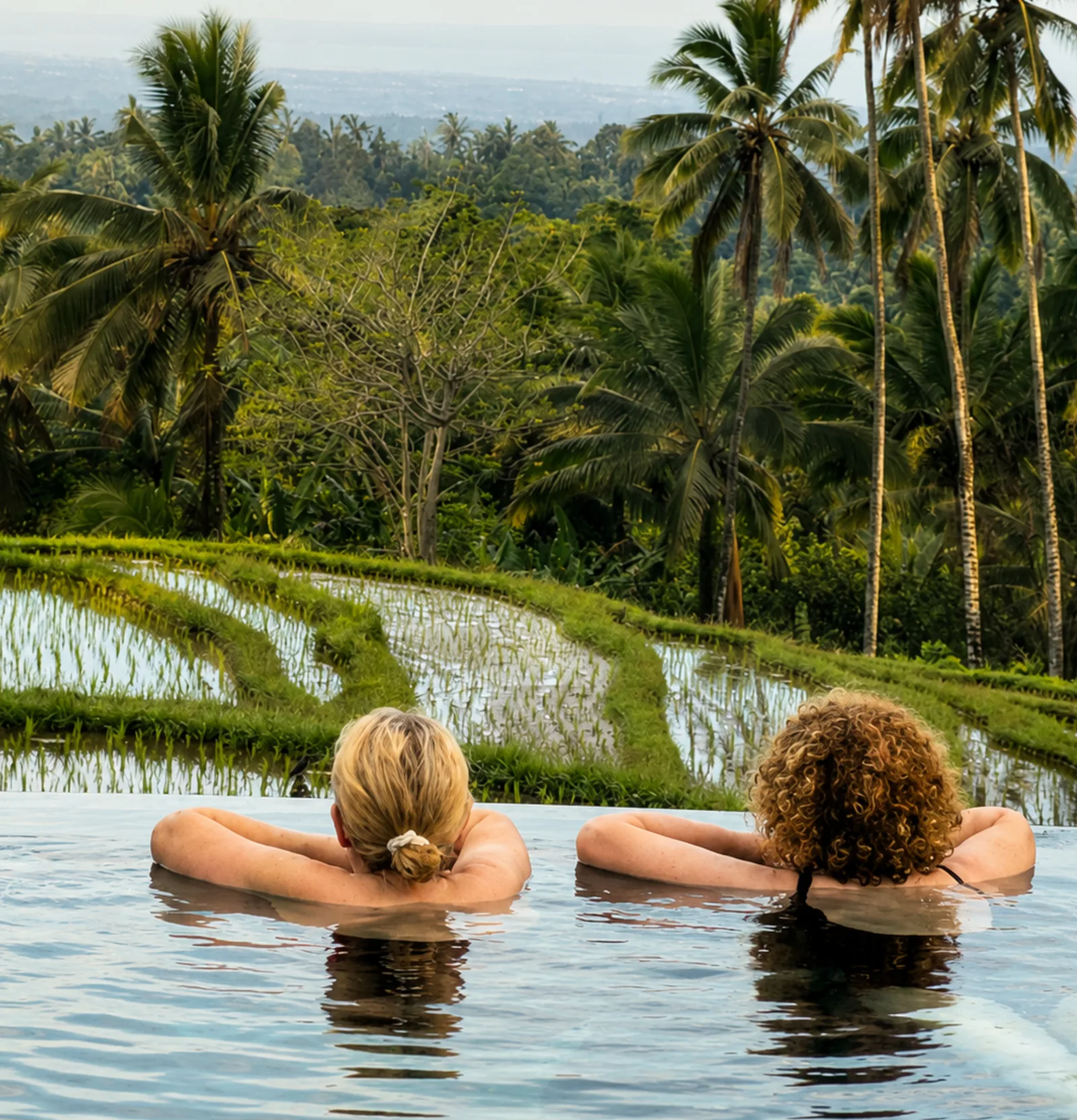 Two women relaxing in infinity pool overlooking Bali rice terraces